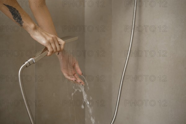 Hands are positioned under flowing water from a sleek showerhead in a stylish bathroom. The setting features clean lines and neutral walls, emphasizing a relaxing ambiance during personal care