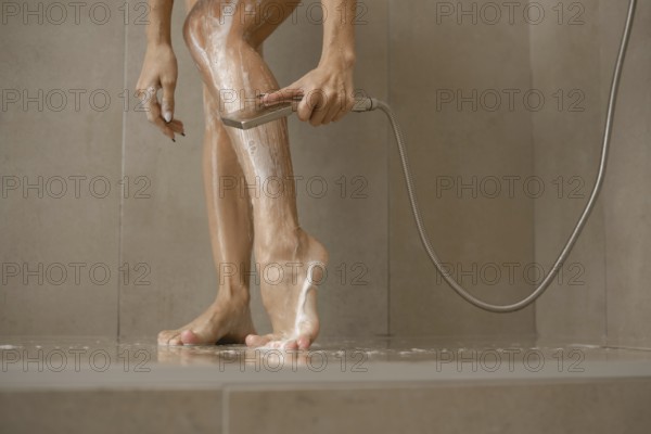 A woman stands in a sleek shower, washing soap off her legs while using a handheld showerhead. Water cascades around her feet, showcasing a fresh start to the day in a serene bathroom setting