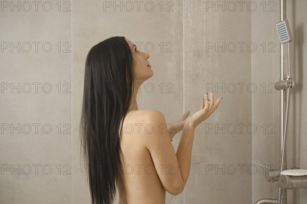 A woman stands underneath flowing water in a minimalist shower, enjoying a moment of peace. The soft lighting highlights her natural beauty as she engages in self-care