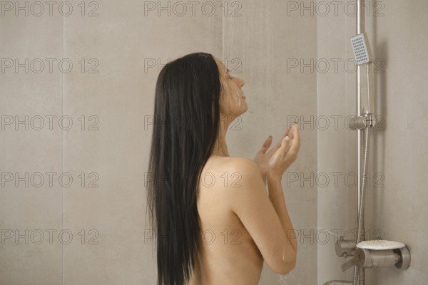 A woman stands under warm water in a contemporary bathroom, her long hair cascading down her back