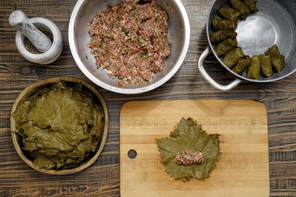 In a cozy kitchen, grape leaves are prepared for making dolma. A mixture of rice and minced meat is being formed into small portions on a wooden board, ready for wrapping in leaves