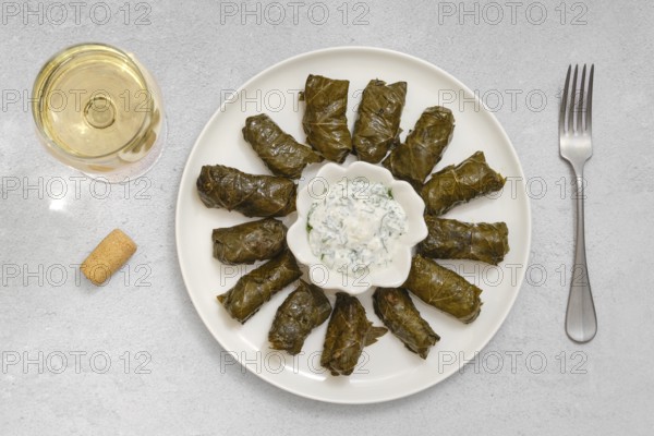 Dolma is being prepared at home, featuring grape leaves stuffed with rice, lamb meat and herbs, served with tangy yogurt sauce