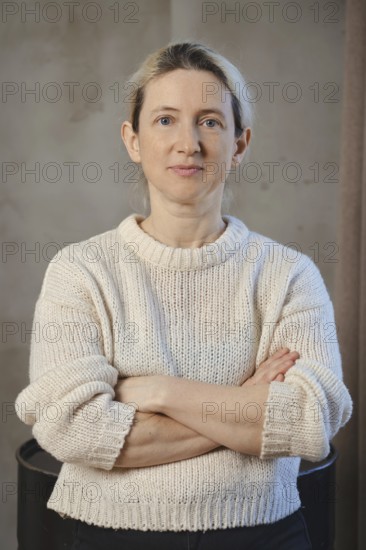 A woman poses confidently with her arms crossed, dressed in a soft, knitted sweater