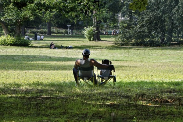 A man sits with his daughter under a shady tree, Berlin, 20 July 2025, Berlin, Germany