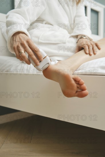 Close-up view of peeling dead skin off heel with handheld electric exfoliating machine in bedroom