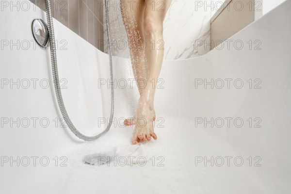 Water cascades from a handheld showerhead as a person stands in a sleek, white bathtub. The atmosphere is calming, showcasing marble tiles and a serene bathing environment
