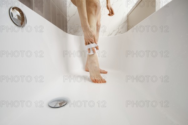 Unrecognizable person washing legs in bathtub of a minimalistic bathroom during a morning routine