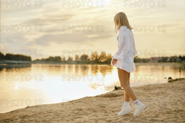 Woman walking on sandy shore during sunset by calm water in peaceful natural setting