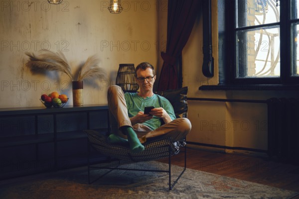 A man sits in a living room and checks a balance using a mobile banking application on smartphone