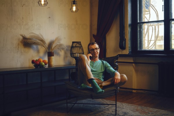 A man is comfortably seated in a modern chair, wearing casual attire with colorful socks