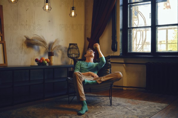 A man sits comfortably in a chair, gazing thoughtfully at an apple in his hand. Soft lighting and elegant decor enhance the peaceful ambiance of the cozy space