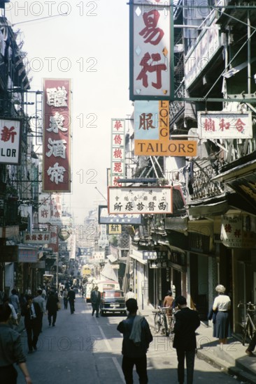 Busy street of shops and signs in English and Mandarin including for Tai Cheong Tailors, Wellington Street, Hong Kong, Asia 1964
