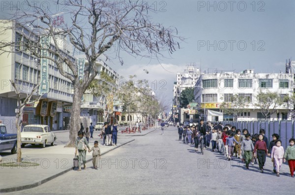 Primary school children walking hand in hand along city centre commercial street, Macau, Asia 1964