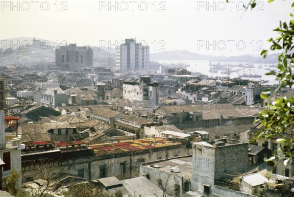View over rooftops of high density buildings in city centre to Our Lady of Penha Chapel on hilltop from Monte Fort, Macau, Asia 1964