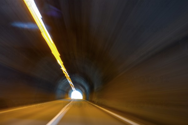 View from car while driving fast on car driver speeding car racer through long tunnel with straight tunnel tube with light at the end of long of a long tunnel above narrow light strips ceiling lighting, international