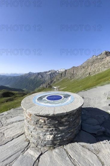 In front orientation board on stone plinth at viewpoint on third highest asphalted pass in the Alps highest border pass in the high Alps Alpine pass above tree line behind it view of southern ramp southern ascent mountain road Alpine road to 2744 metre high Col d'Agnel, Colle dell'Agnello, Pontechianale, Piedmont, Italy
