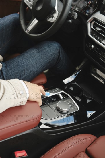 A person in casual attire sits in the driver's seat of a modern vehicle, reaching to adjust the controls located on the center console