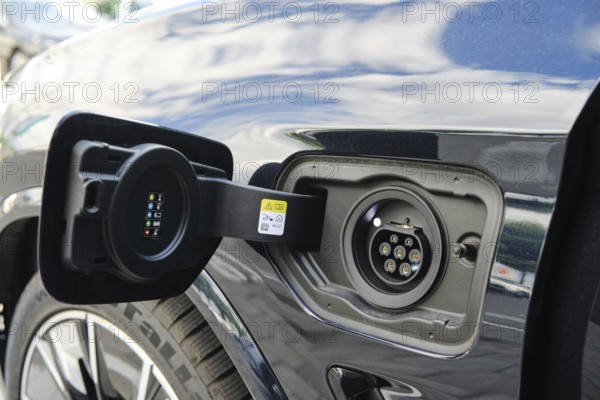 Close-up view of electric vehicle charging port during bright daytime at urban charging station. The bright sky reflects on the vehicle's surface, showcasing modern design and technology