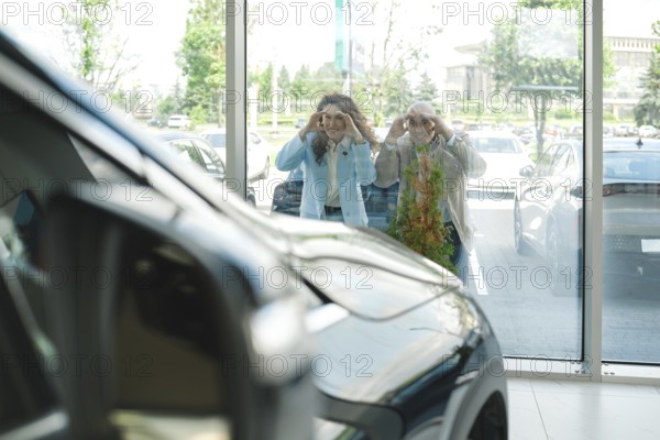 Couple put their hands on the glass peering through large windows at car showroom