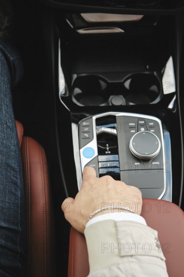 A driver is adjusting the controls in a luxury vehicle. The focus is on the comfortable leather seat and the sleek, modern dashboard design