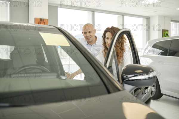 A couple is exploring options at a car dealership, looking closely at a vehicle. They appear engaged in discussion, evaluating features and making decisions on their potential purchase