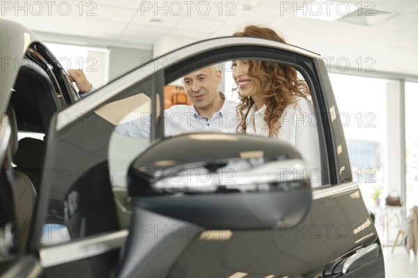 A customer enjoys a discussion with a salesperson while inspecting a vehicle at a busy car dealership. The bright, welcoming atmosphere encourages exploration and decision-making