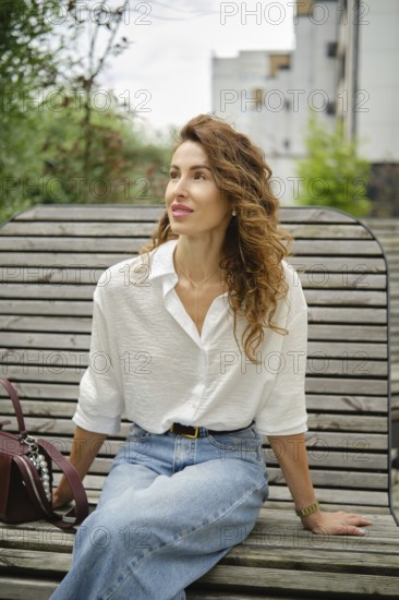 Woman sitting on a bench in a park, enjoying her surroundings during a sunny afternoon