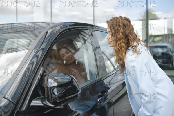 A woman inspects a sleek black car at a dealership, admiring her reflection in the glossy surface as she considers her options. Bright natural light fills the space, enhancing the experience, AI generated