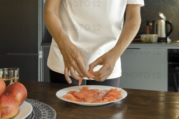 A person is arranging fresh salmon slices on a white plate in a stylish kitchen showcasing a focus on nutritious food preparation