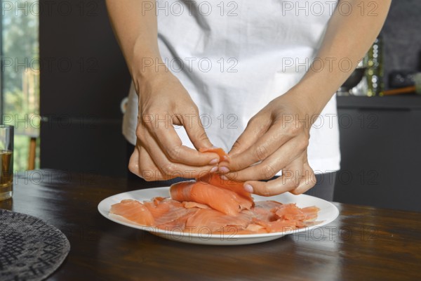 Hands expertly handle smoked salmon fillets on a plate, showcasing a focus on healthy food preparation. Natural light streams in, highlighting the vibrant colors of the dish