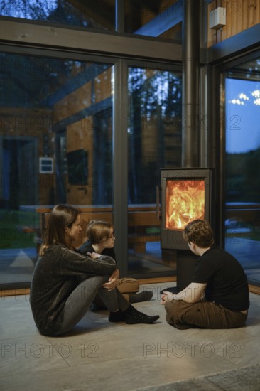 A family of three gathers around a glowing fireplace inside a contemporary cabin. The warm ambiance contrasts with the cool evening outside, creating a relaxed atmosphere for quality time together