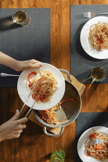 Close-up view of female hands serving pasta with stir fry spicy beef with vegetables on a plate