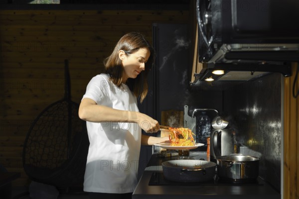 A woman takes out fried vegetables from the pan with kitchen tongs standing by the stove in a kitchen filled with natural light