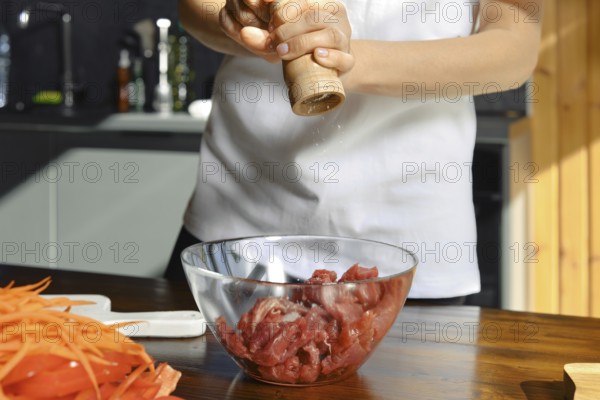 Unrecognizable person is adding freshly ground salt to a bowl of diced meat, preparing for a healthy meal