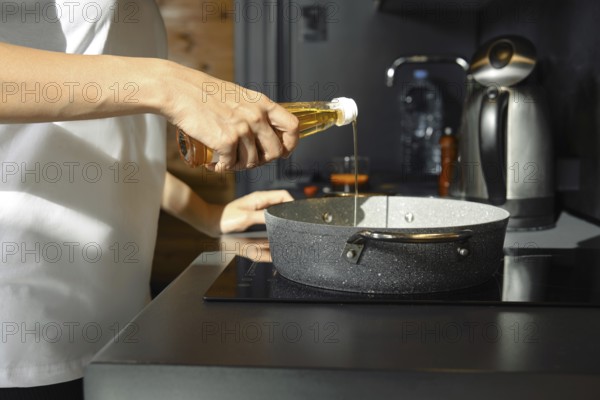 A person pours sesame oil into a saucepan while preparing a healthy meal in a modern kitchen. The warm lighting complements the sleek appliances, indicating a focus on nutritious cooking