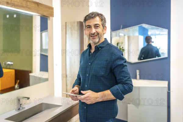 Smiling mature male architect using a digital tablet while choosing bathroom fixtures in a home improvement store showroom