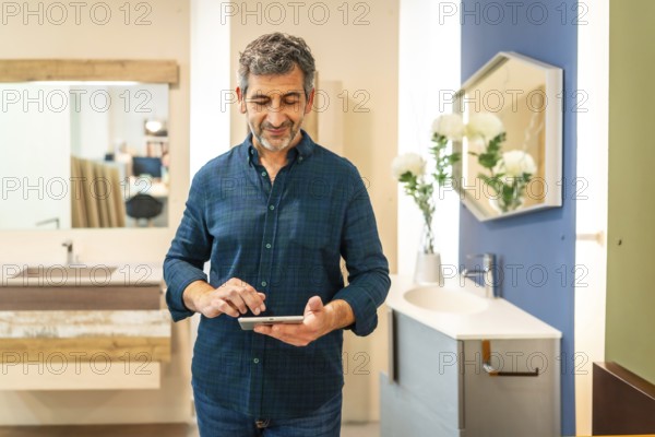 Mature architect using digital tablet choosing bathroom fixtures in home improvement store, smiling and checking some details
