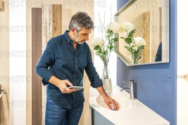 Architect using tablet while checking bathroom sink in home improvement store, evaluating materials for new project
