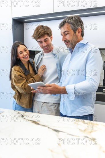 Smiling interior designer showing digital tablet to laughing couple while working in modern kitchen showroom
