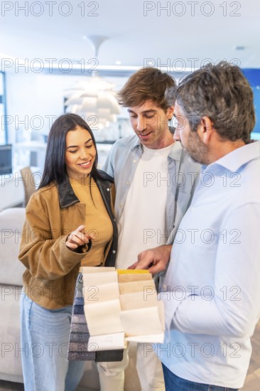 Couple choosing upholstery fabric from a wide variety of swatches held by a home improvement store salesperson
