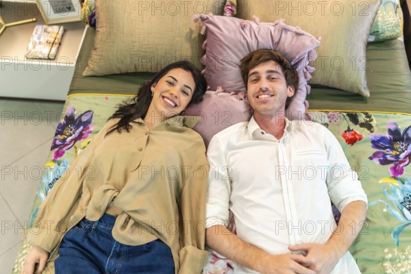 Young couple smiling and lying on a bed, testing comfort together while shopping for home goods in a vibrant home improvement store