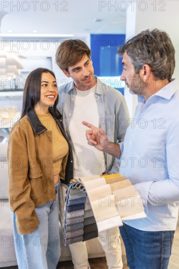 Couple and interior designer choosing upholstery fabric, holding samples in a furniture store showroom