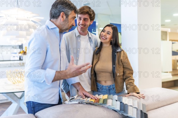 Couple and salesman discussing upholstery fabric swatches in furniture store, exploring options for their home decor
