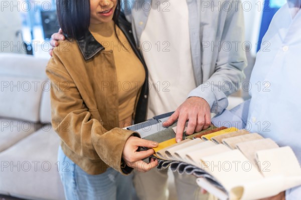 Couple browsing through a catalog of upholstery swatches while consulting with a furniture store salesman on fabric options for their home