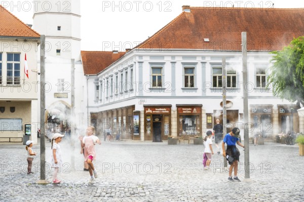 Water mist system in the city centre of Trencin, children use the refreshment in the summer heat, Trencín, Slovakia