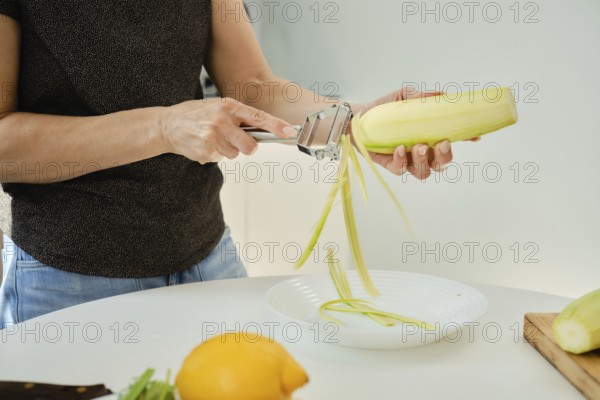 Unrecognizable woman skillfully cuts zucchini into strips with a hand-held tool and cooks vegetable noodles in a bright kitchen