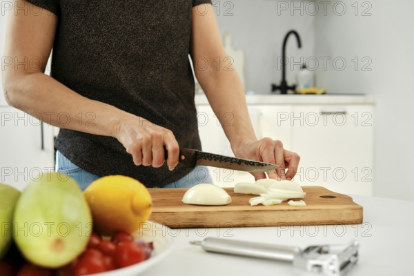 A person is slicing fresh onion on a wooden cutting board in a sleek kitchen. Colorful fruits and vegetables are arranged in a bowl nearby, adding vibrancy to the workspace