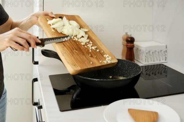 An unrecognizable woman laid out chopped onions and garlic in a frying pan. She is preparing the base for main course