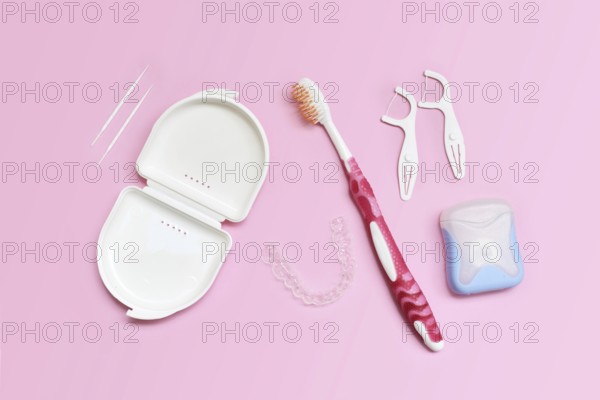 Top view of dental clear aligners, toothbrush, toothpicks and floss on pink background with copy space