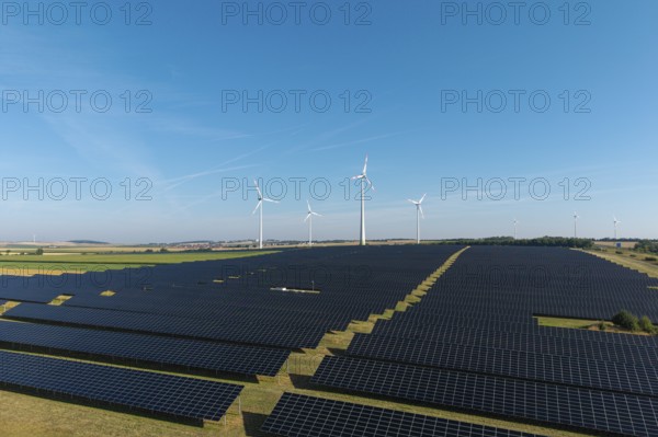 Field full of solar panels with wind turbines in the background under a clear sky, near Kitzingen, Lower Franconia, Bavaria, Germany